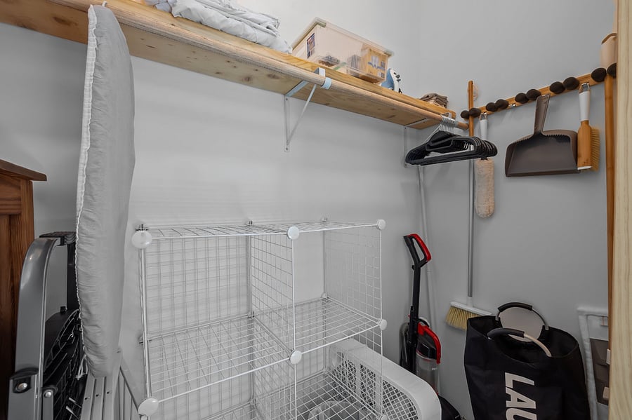 The closet interior includes a dresser, laundry essentials, compact ironing board & iron, hangers, basic cleaning equipment including a vacuum, basic cleaning supplies, laundry hamper & basket, box fan, & extra storage shelves.