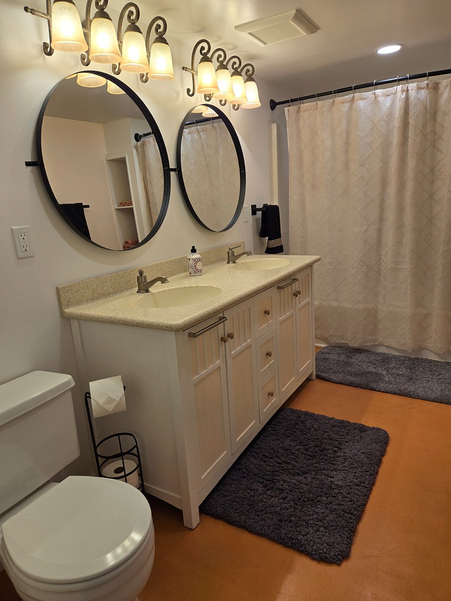 Double vanity with accent lighting. Bathtub/shower behind the curtain and toilet to the left of the sink.