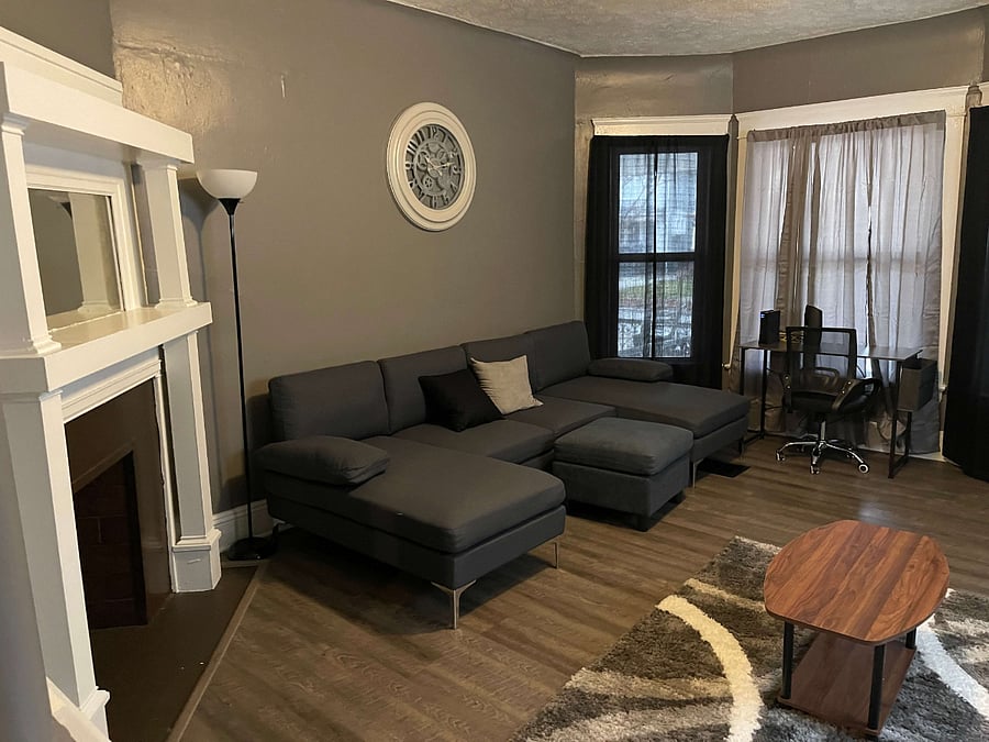 The living room in this unit is a spacious and elegantly designed area that invites relaxation and social interaction. It features two plush couches and a chaise lounge, perfect for unwinding or hosting guests. The central coffee table and accompanying ottomans offer both style and functionality, complementing the soft area rug that adds warmth to the space. For those needing to catch up on work, the room also includes a desk and an office chair, creating a convenient workspace that blends seamlessly with the rooms relaxed ambiance.