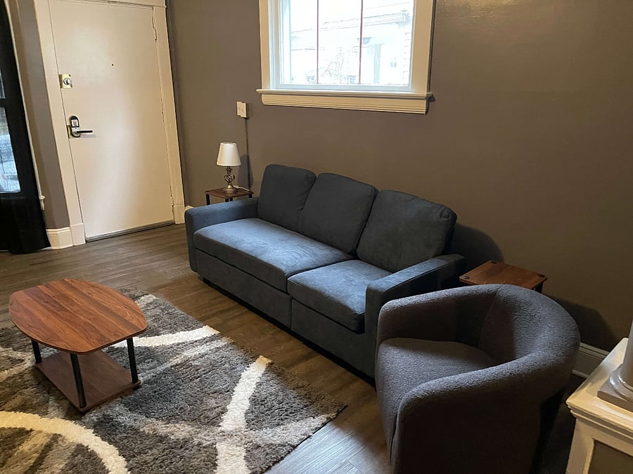 Step into the inviting ambiance of this generously sized living room, where comfort meets contemporary style. Two cozy couches and a stylish chaise lounge provide ample seating for relaxation or entertaining. The layout is centered around a chic coffee table, flanked by versatile ottomans, making it ideal for evening chats or morning coffee. An attractive area rug anchors the space, enhancing its welcoming feel. Additionally, a desk and office chair are thoughtfully placed, offering a practical spot for work without leaving the comfort of the living area.