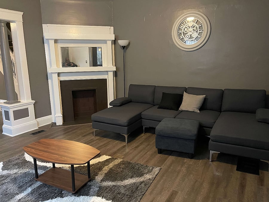 Discover a warm and welcoming living room setup, ideal for relaxation and social activities. Furnished with two plush couches and a matching ottoman, this space invites comfort and ease. An elegant area rug anchors the room, while end tables with lamps provide soft lighting. A dedicated workspace with a desk and office chair ensures productivity, and the central coffee table is perfect for hosting or casual use.
