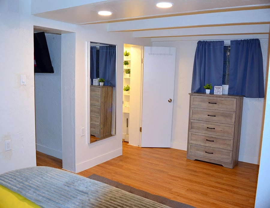 This spacious bedroom features a dresser for ample storage, a full-length mirror and an ensuite bathroom.