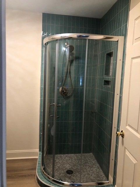 Tile shower, with rain water head and enclosed glass doors. With hooks to hang towels.