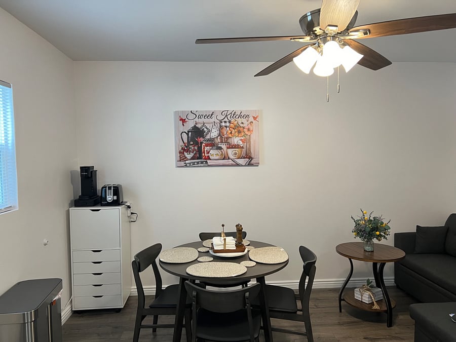 Dining area with woven placemats, starter napkins, and a starter salt and pepper set. Dining room is connected to living room and kitchen.