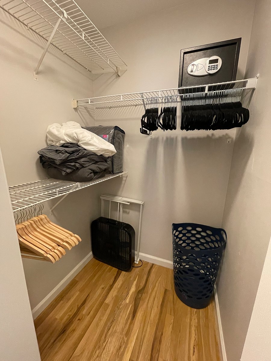 Walk-in closet with plenty of hangers, extra bedding, box fan, laundry drying rack, and safe