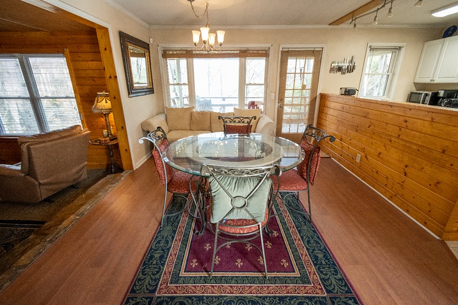 Landscape view of the dining area, entry to the living room and glimpse of the kitchen. Back door leading to deck can be found in the background.