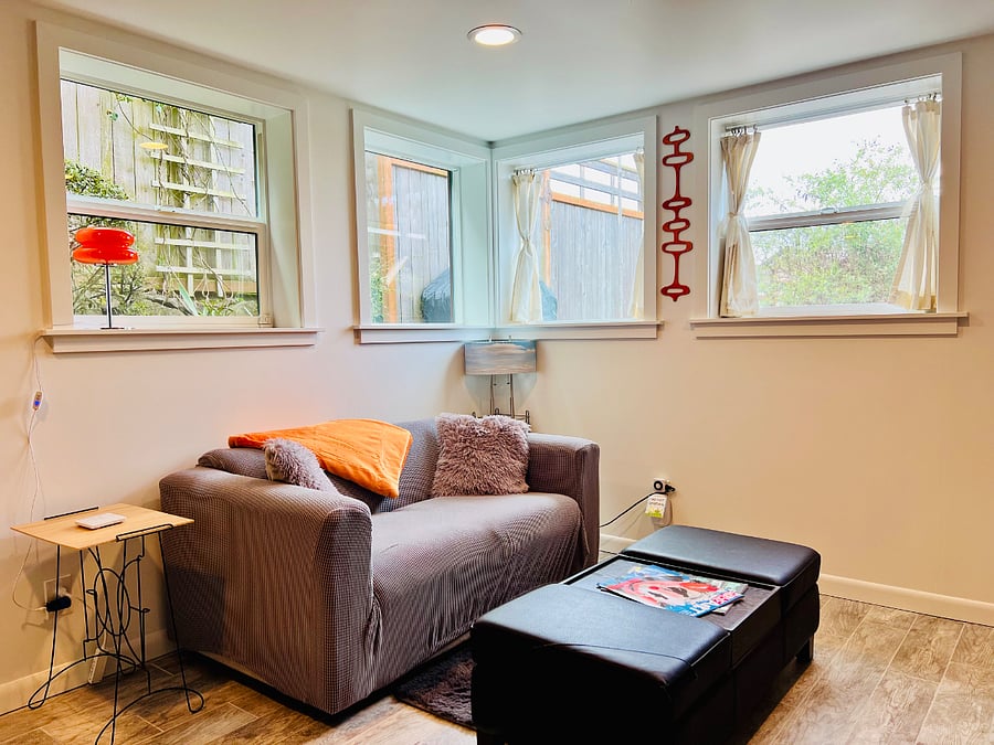Living room with comfy loveseat, ottoman coffee table, very private views of English Rose Garden from kitchen and living room. Curtains optional.