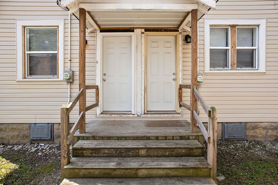 Front entrance of a duplex with wooden stairs and railings leading to two white doors.