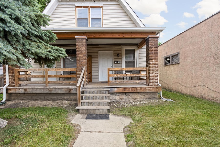 Welcoming front porch with classic brick columns and a spacious yardideal for a cozy home vibe!