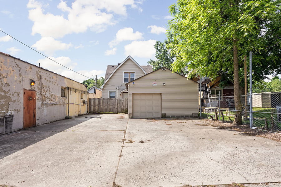 Spacious backyard with a concrete driveway, detached garage, and surrounding fences, featuring a mix of residential and commercial structures.