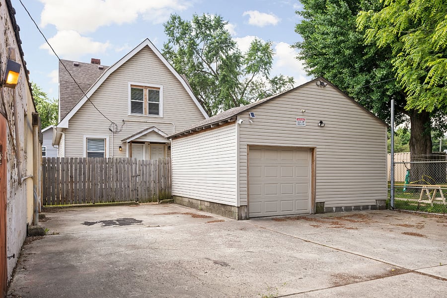 Concrete driveway leading to a detached garage, with a fenced backyard and a residential home in the background.