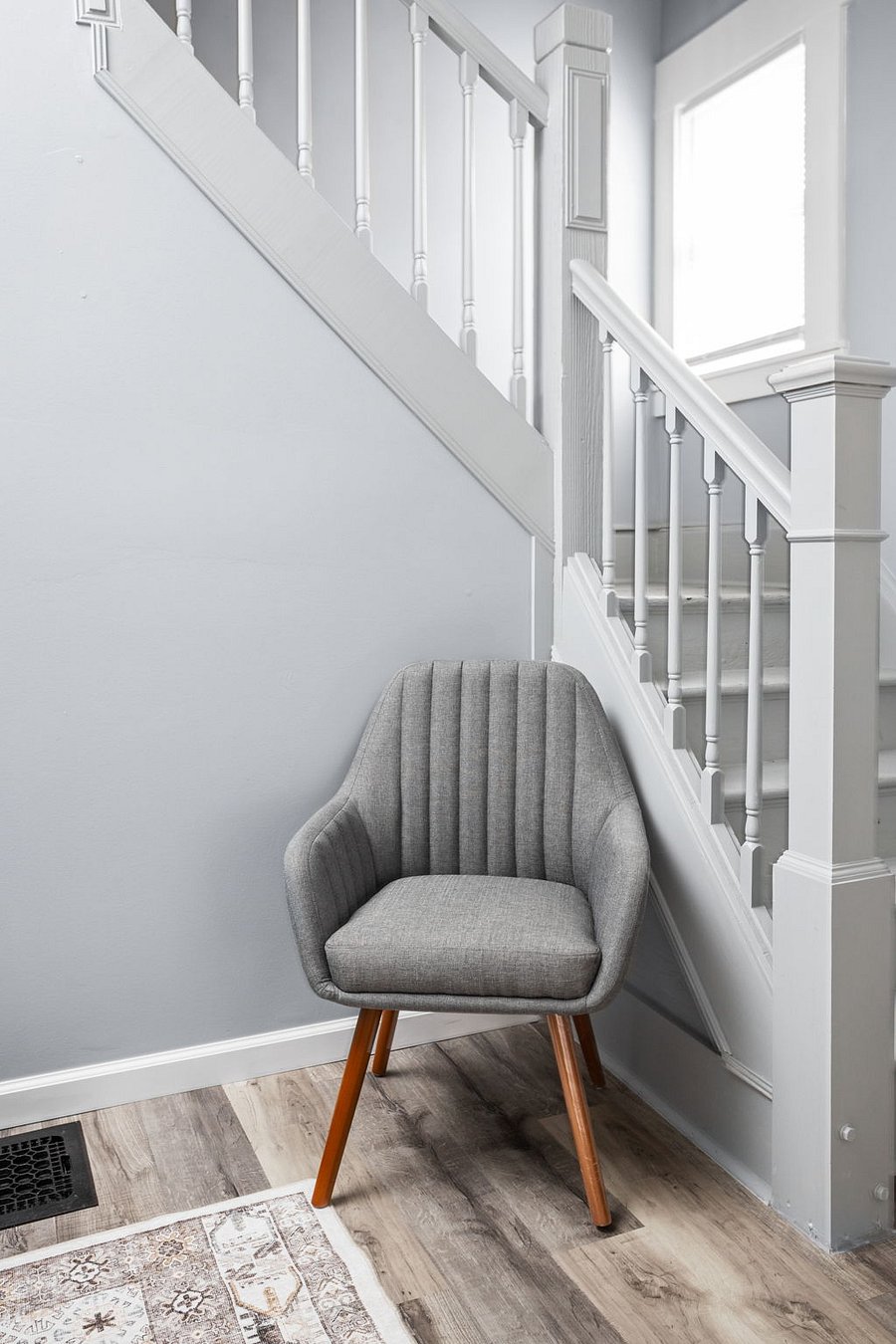 Cozy reading nook with a stylish gray accent chair tucked beside a white staircase.