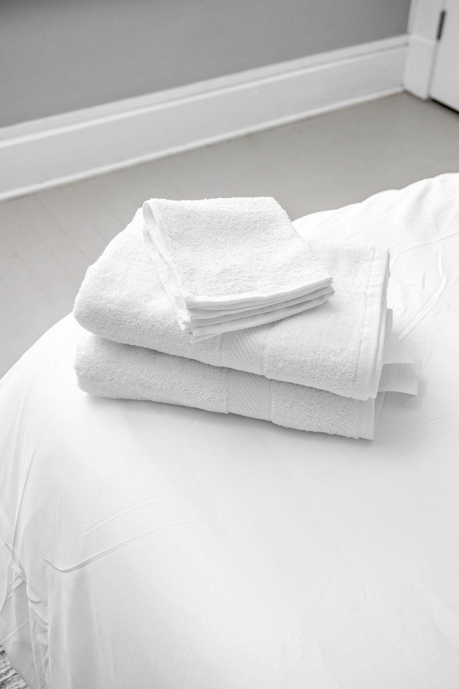 Neatly folded white towels placed on a freshly made bed, creating a clean and inviting atmosphere.