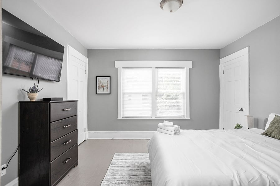 Bright and modern bedroom with minimalist decor, a mounted TV, and fresh linens for a cozy stay.