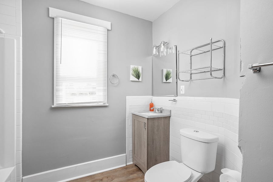 Bright and modern bathroom with gray walls, white subway tiles, a compact vanity, and a large window for natural light.