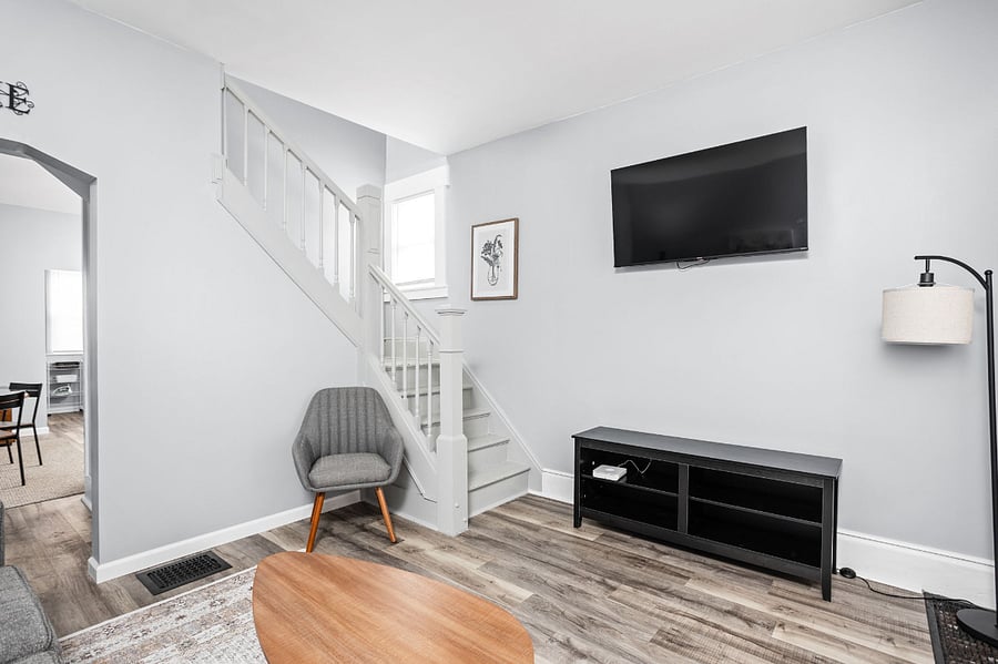 Modern living room with a mounted TV, a cozy gray accent chair by the staircase, and a sleek entertainment console.