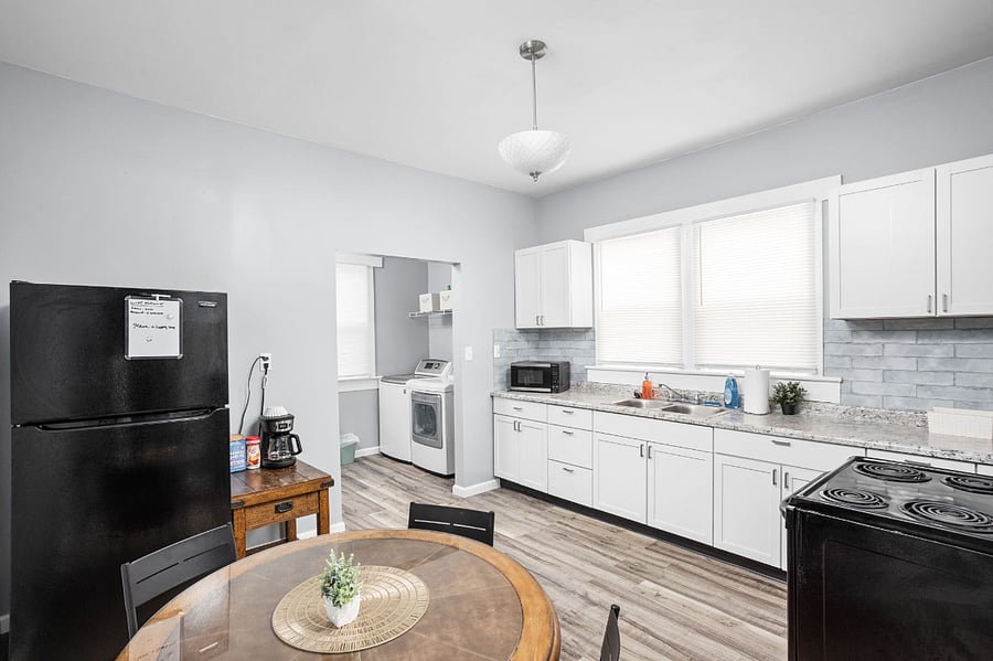 Bright and spacious kitchen with white cabinetry, black appliances, a round dining table, and an open doorway leading to a laundry area.