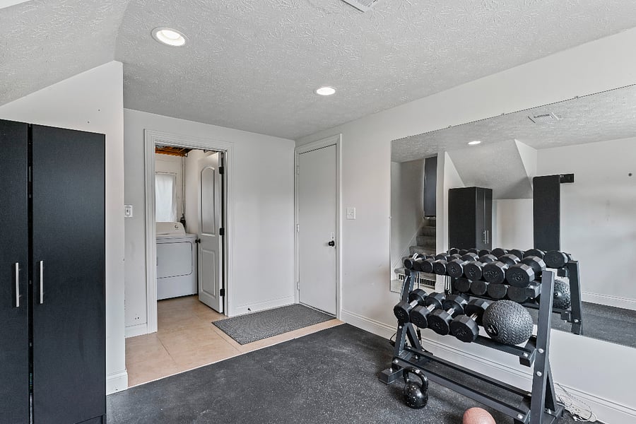 A lower-level fitness room with a garage entry provides convenience and accessibility for fitness enthusiasts. The incorporation of a garage entry allows for easy access to the fitness space without disrupting the main residence. Additionally, having a laundry room adjacent to the fitness room offers practicality for gym-goers to easily clean their workout clothes. The inclusion of a half bath ensures that individuals can freshen up post-workout without needing to go upstairs. This integration of spaces creates a functional and efficient area for both exercise and everyday tasks.