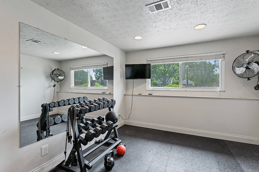 The space features a full dumbbell rack, providing a wide range of weights for various exercises. The gym flooring is designed to withstand heavy equipment and high-impact movements, ensuring a durable and safe workout surface. A large workout mirror helps individuals maintain proper form and technique during exercises. The wall-mounted TV offers entertainment or workout videos to keep users motivated. A fan provides ventilation and keeps the space cool during intense workouts. Lastly, the large opening window brings in natural light and fresh air, creating an invigorating and energizing atmosphere for a productive exercise session.