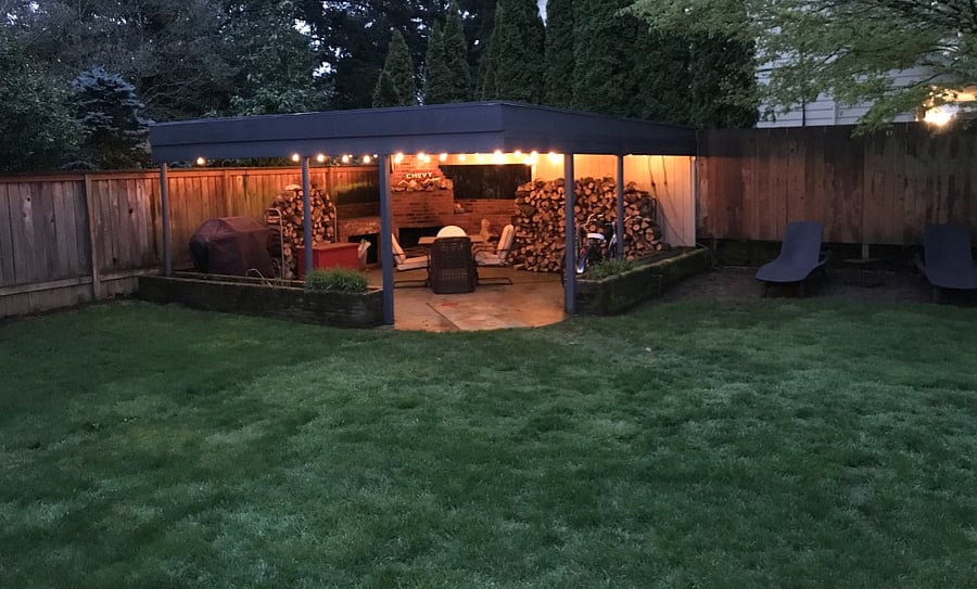 Backyard covered patio, 20' x 20', with fireplace & firewood, grill, sofa & chairs, table, lights, and more.