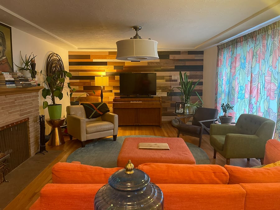 The living room has a fireplace, large tv, piano and plenty of seating. There is a center ceiling light with fan inside. There are extra blankets in a silver trunk behind the chair. There is a cabinet with games.