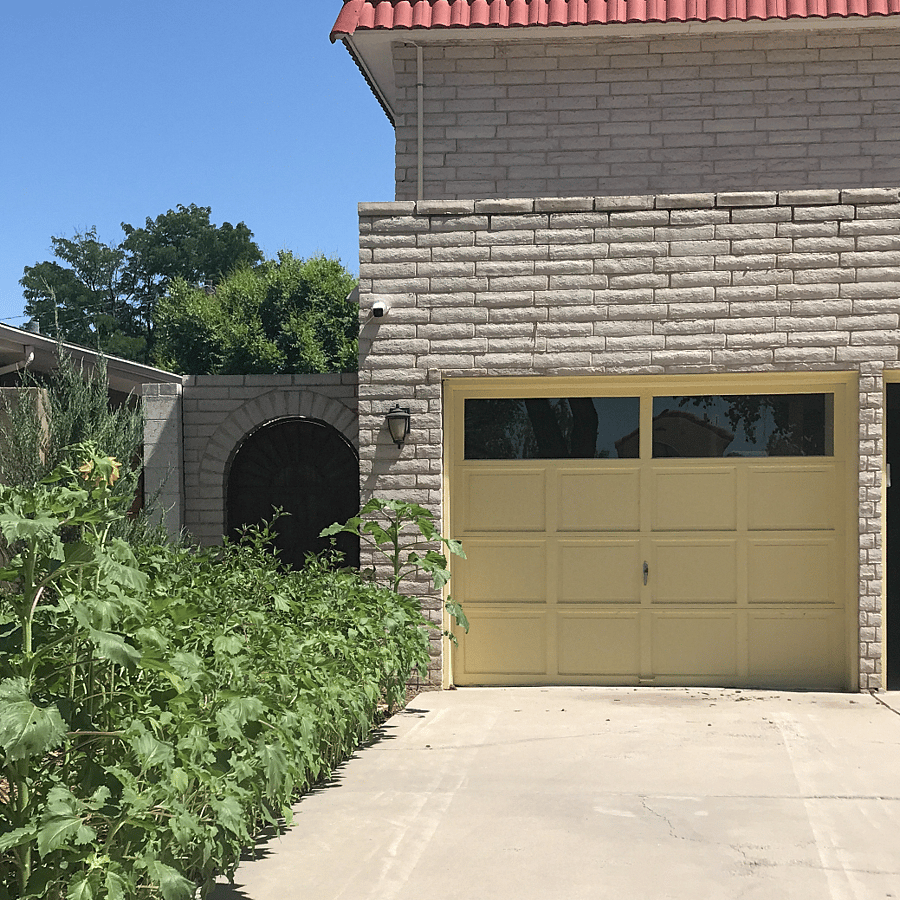 Tenant parking space, flanked by sunflowers. Room over garage is room that is being rented.