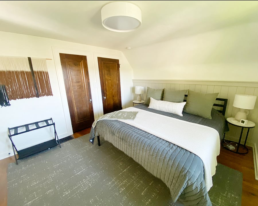 The second upstairs bedroom features a king bed with plush bedding, a dedicated workspace, and a twin fold-out mattress tucked away in one of two closets. A full bathroom with a tiled walk-in shower is just steps away.