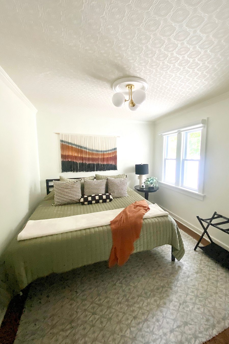 The first floor bedroom features a king bed and soft bedding, a wall mirror, a closet with hangers, and a luggage rack. A large window offers a lovely view of the back patio, and a full bathroom with a tiled walk-in shower is just steps away.