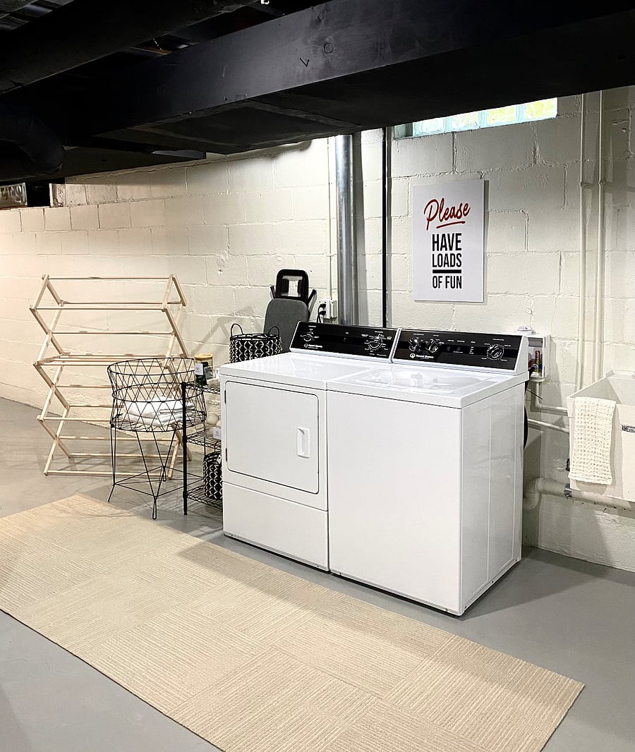You'll appreciate the fully equipped basement laundry area, complete with starter supplies, an iron and ironing board, and a clothes rack. To the right of the washing machine, a utility sink adds convenience to your laundry routine.