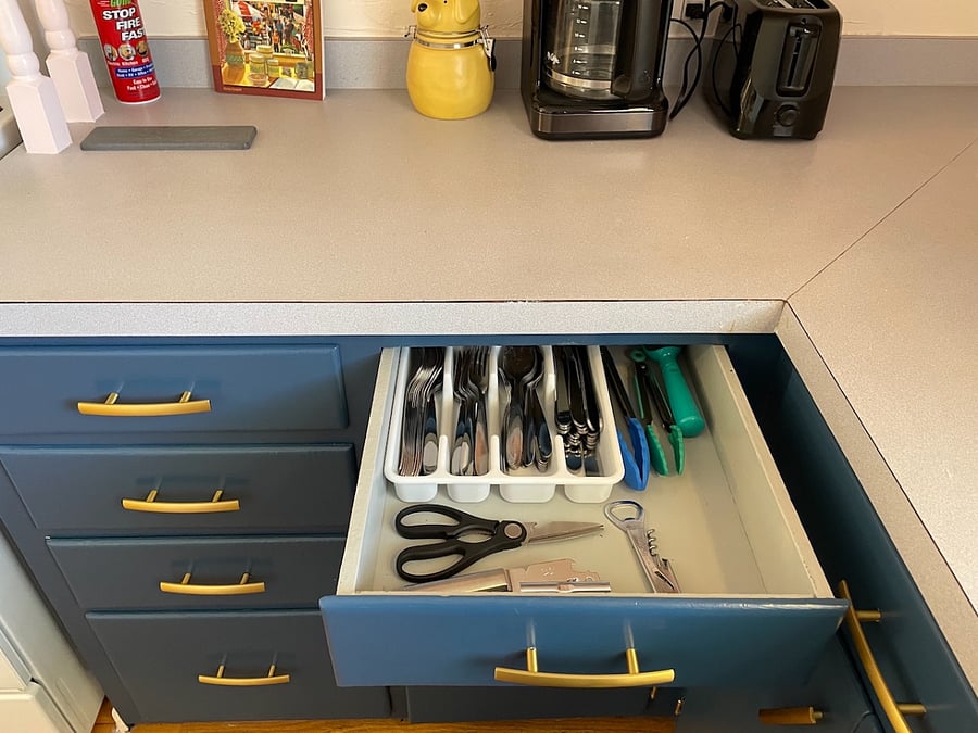 In the top drawer, on the right side of the south wall, you'll find cutlery, tongs, a can opener, bottle opener, an ice cream scooper, and kitchen scissors.