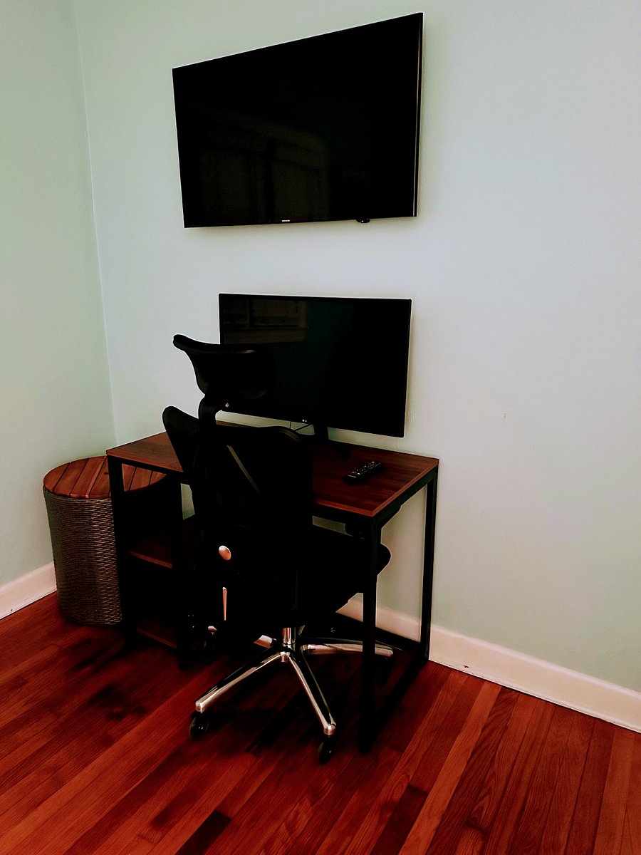 Office features comfortable office chair; monitor; smart TV; table lamp; chair & ottoman. 