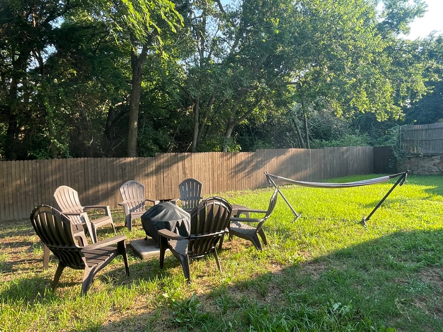 Backyard fire pit area and hammock under a canopy of trees.