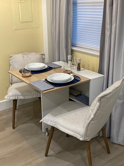 Dropleaf dining table with 2 chairs, place settings for 4, and storage shelf.