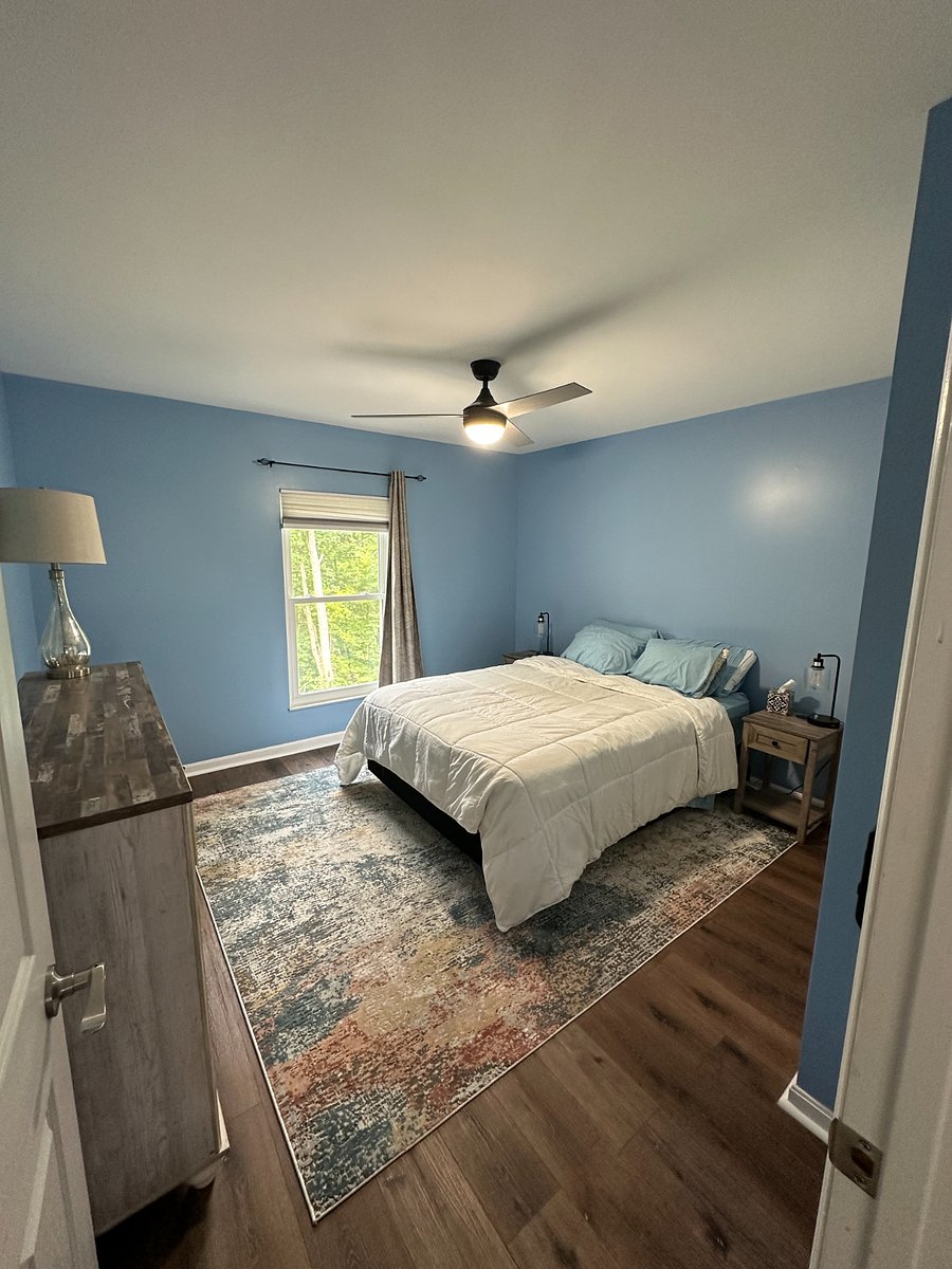 Upstairs guest bedroom with queen sized bed, dresser, and phone-charging end tables. Window faces the back of the house.