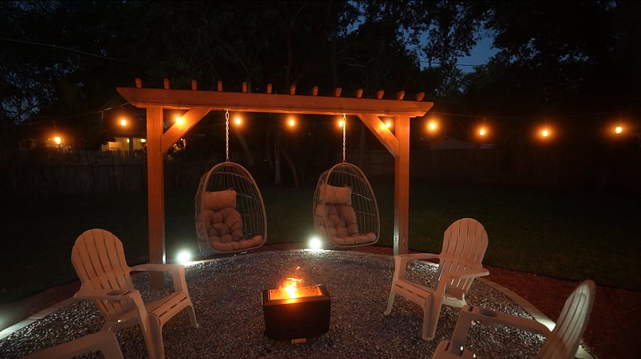Experience your backyard space with warm amber cafe lighting, inviting swing chairs surrounding a cozy fire pit. 