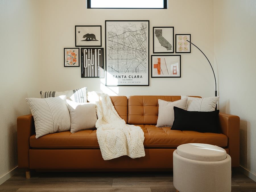 Relax on the leather couch beneath the California art gallery wall. Ottoman triples as footrest, storage, and table.