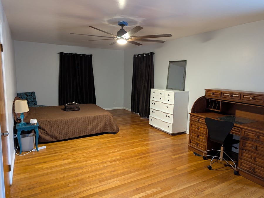 Master bedroom is approx 435 sqftwith blackout curtains, roll top desk, dresser and mirror. Curtains closed.