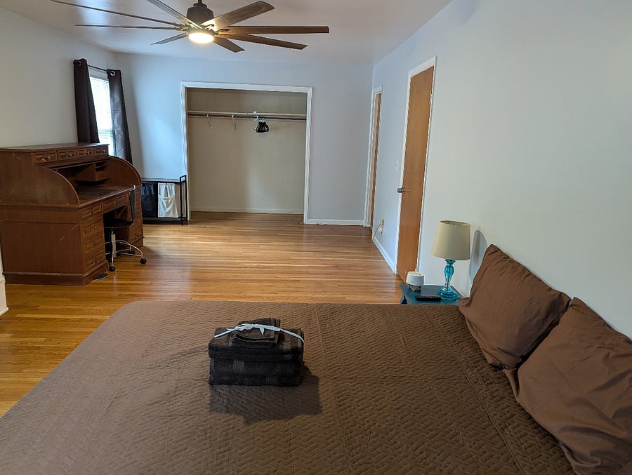 Master bedroom is approx 435 sqft with blackout curtains, roll top desk, dresser and mirror. Curtains open.