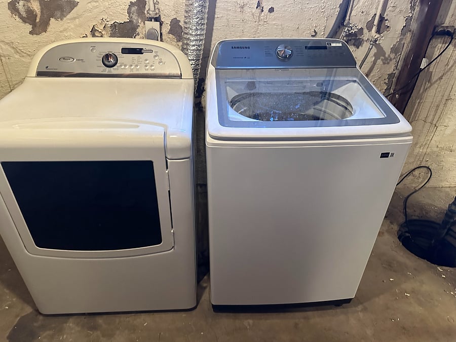 Full sized washer and dryer in basement with supplies