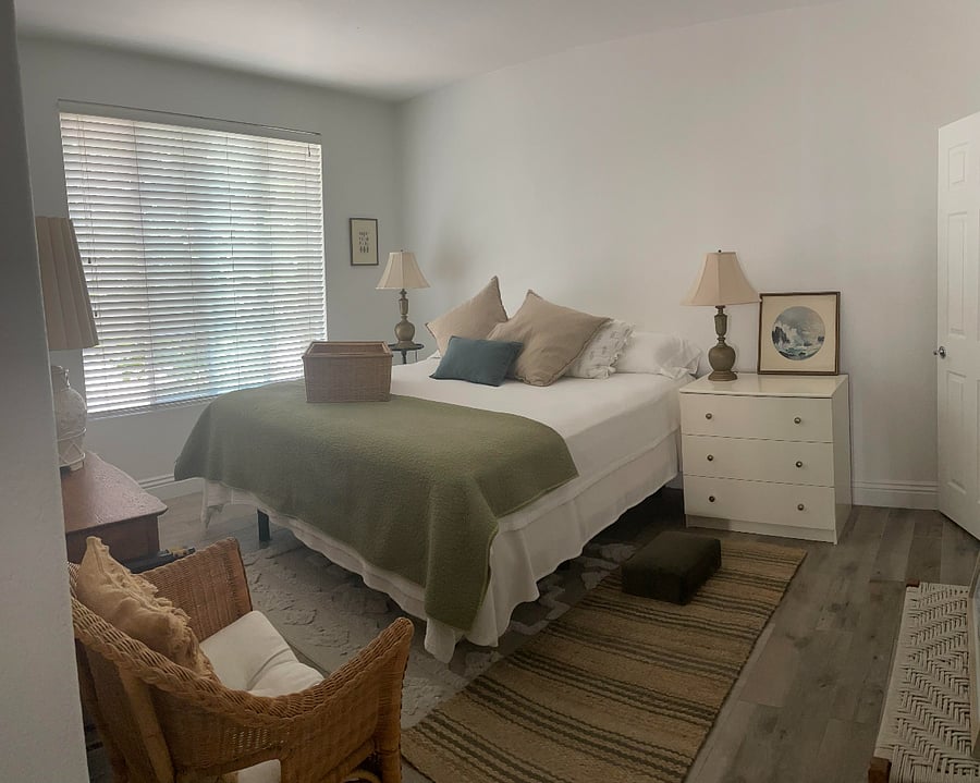 The serene primary includes two chairs, a bench, a small/tall side table near the window, and a new king bed and base. This image includes the three lamps in the room, along with the two dressers that appear in all of the photos. A runner or rug is provided on one side of the bed. Some artwork may not be as pictured.