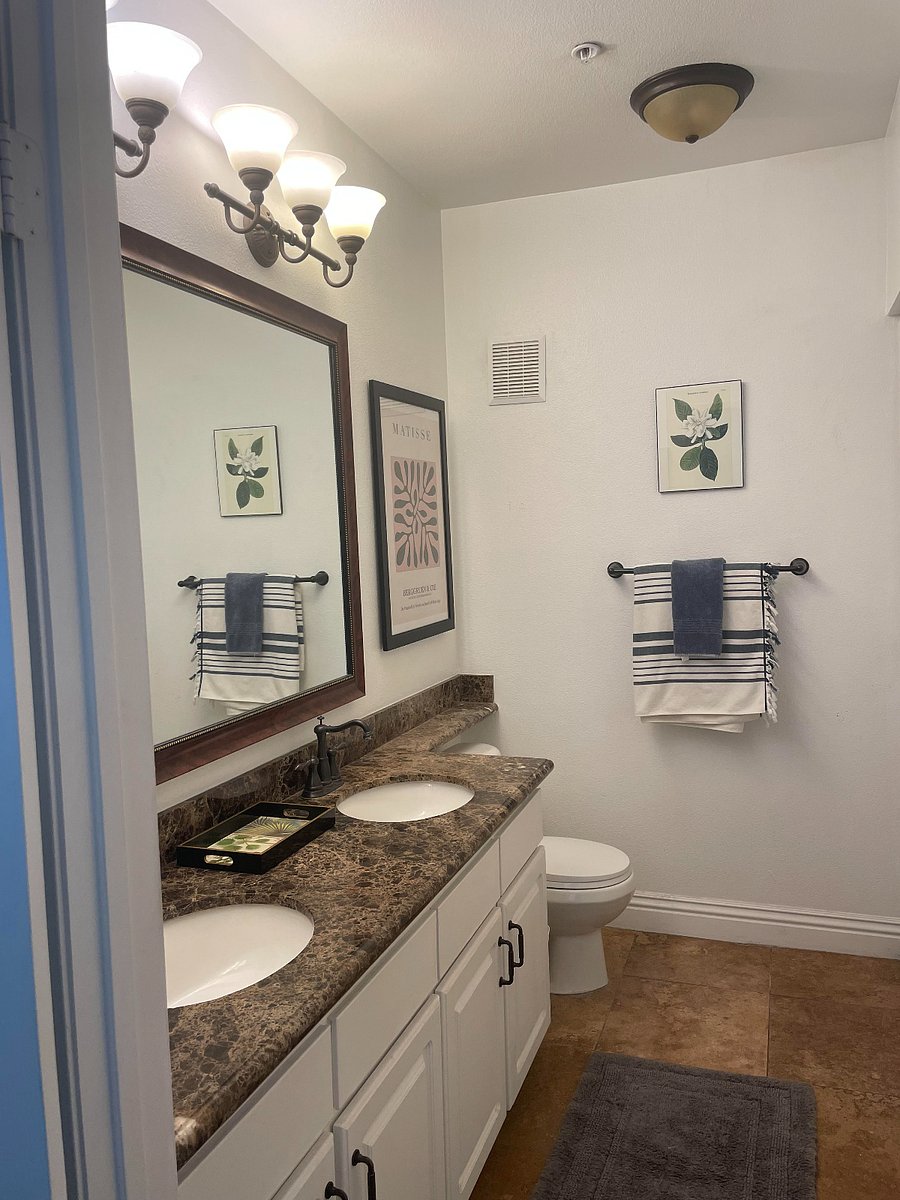 Full primary bathroom with ample storage under sinks and wall cabinet. Artwork on walls, towels, bath mat, and rug provided along with a starter kit.