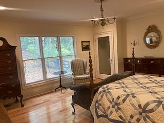 BR2: double bed, sitting area with desk, chair, love seat, wingback chair, dresser, large closet & northern view of private wooded setting.