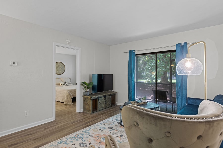 The living room features a cozy seating area, a smart TV, and access to a private screened porch with serene outdoor views.