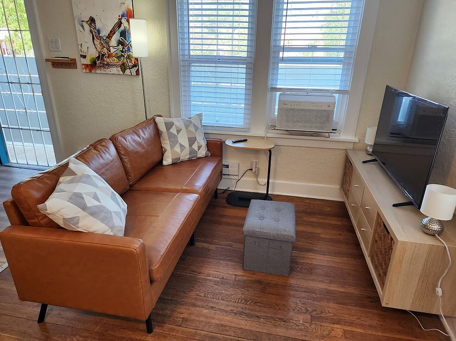 The cozy living room features a leather love seat, a storage ottoman that can serve as extra seating, a side table and smart TV from streaming.