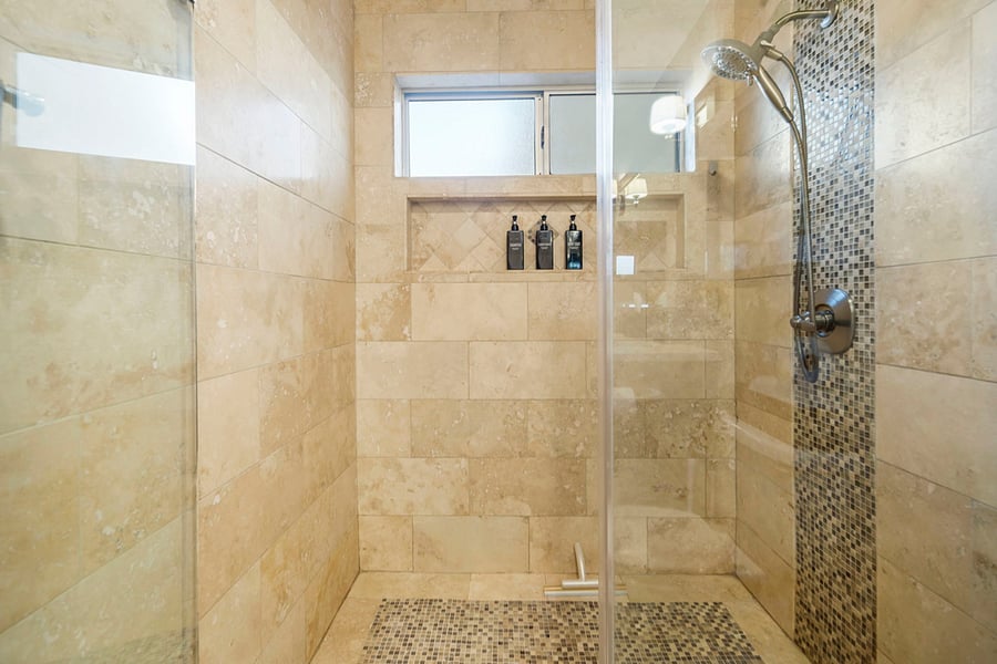 A spacious walk-in shower with sleek glass doors, tiled walls, and a multiple spray option handheld shower head. It features recessed shelving for toiletries, creating a luxurious, open, and functional bathing experience.
