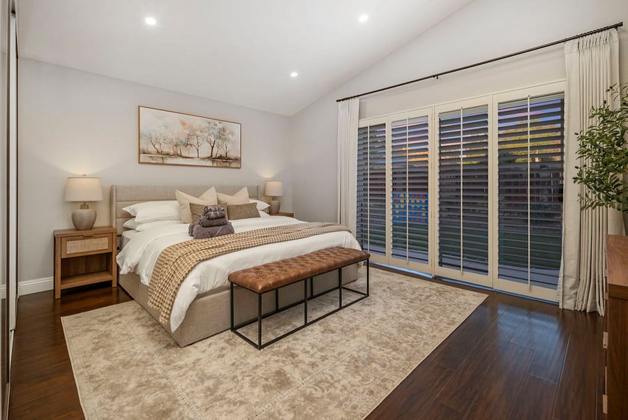 The primary bedroom showcases a king-size bed and sliding doors that open to the backyard, flooding the space with natural light. The seamless indoor-outdoor flow enhances the rooms airy, serene atmosphere, perfect for a relaxing retreat.