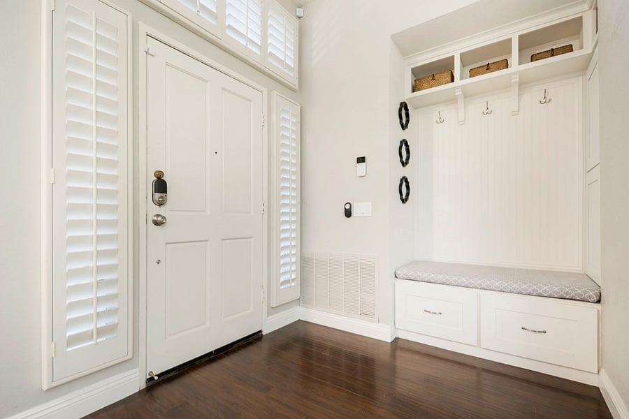 An inviting entrance door opens to a mudroom with ample storage, featuring built-in cabinets and shelves for shoes and bags. Hanging hooks line the walls for coats and hats, creating a tidy, organized space thats both functional and welcoming.
