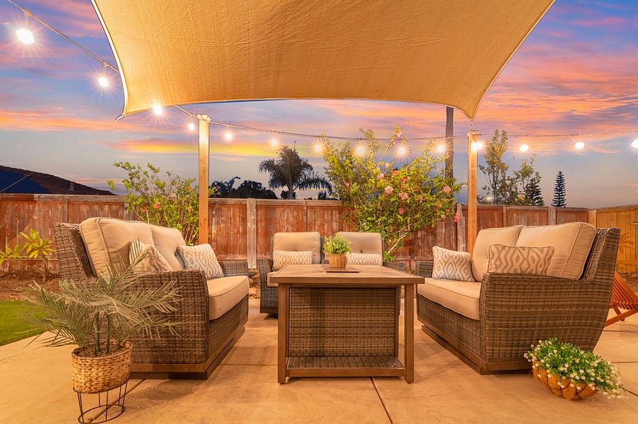 The patio set, right outside the dining room sliding doors, sits under a sunshade sail and is softly illuminated by patio lights. This inviting space blends seamlessly with indoor-outdoor living, perfect for dining or relaxing.