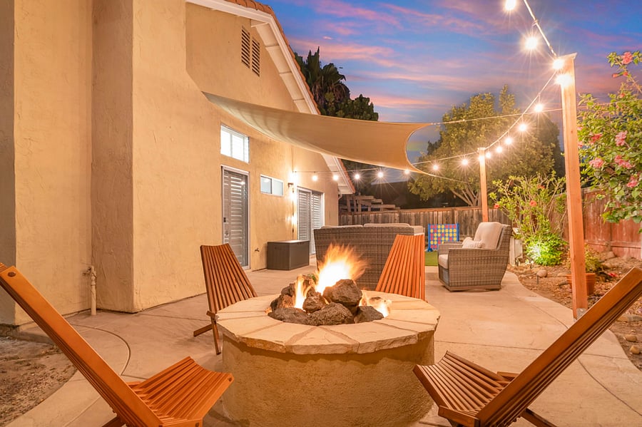 The fully fenced corner lot backyard is a charming retreat with a landscaped garden, a cozy fire pit, and a patio set for gatherings. Twinkling patio lights and a sunshade sail add ambiance and comfort, making it perfect for outdoor relaxation.