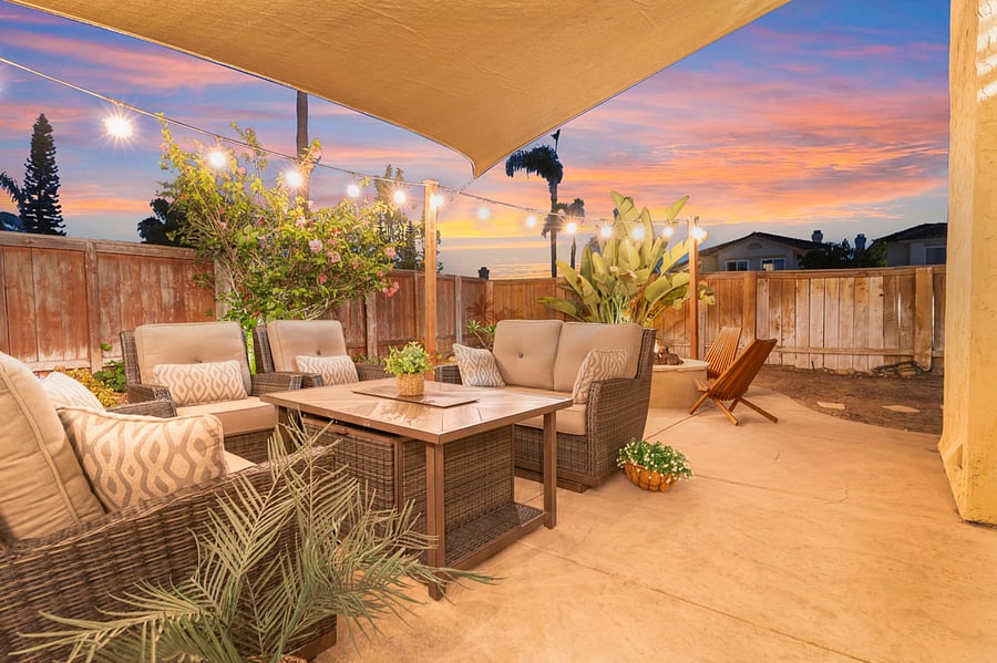 The patio set features charming rocking chairs nestled under a sunshade sail. Patio lights cast a soft glow, creating a cozy, inviting space for relaxation. It's an ideal spot for unwinding and enjoying the serene backyard ambiance.